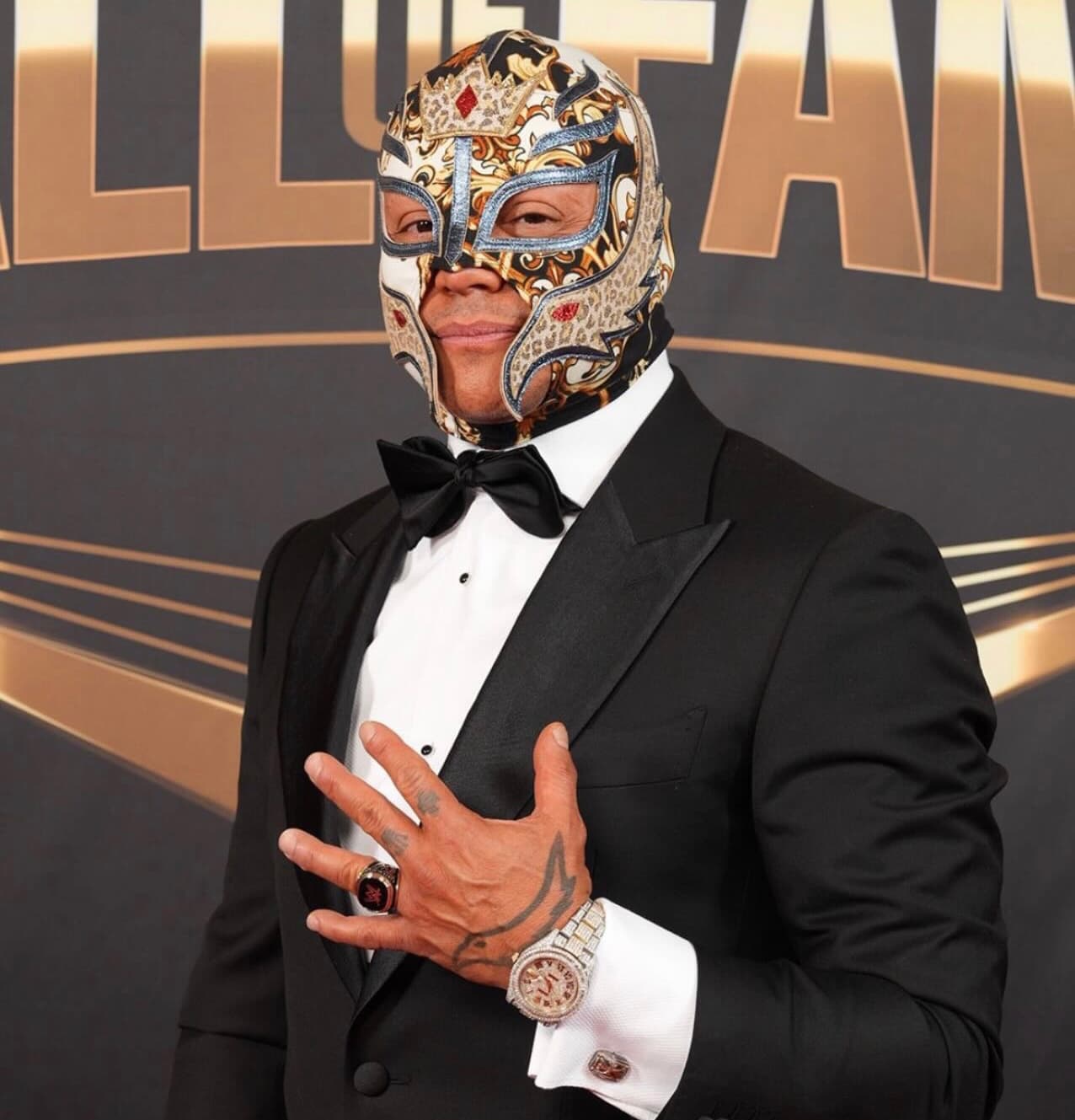Rey Mysterio wearing a decorative mask and tuxedo, posing at the WWE Hall of Fame.