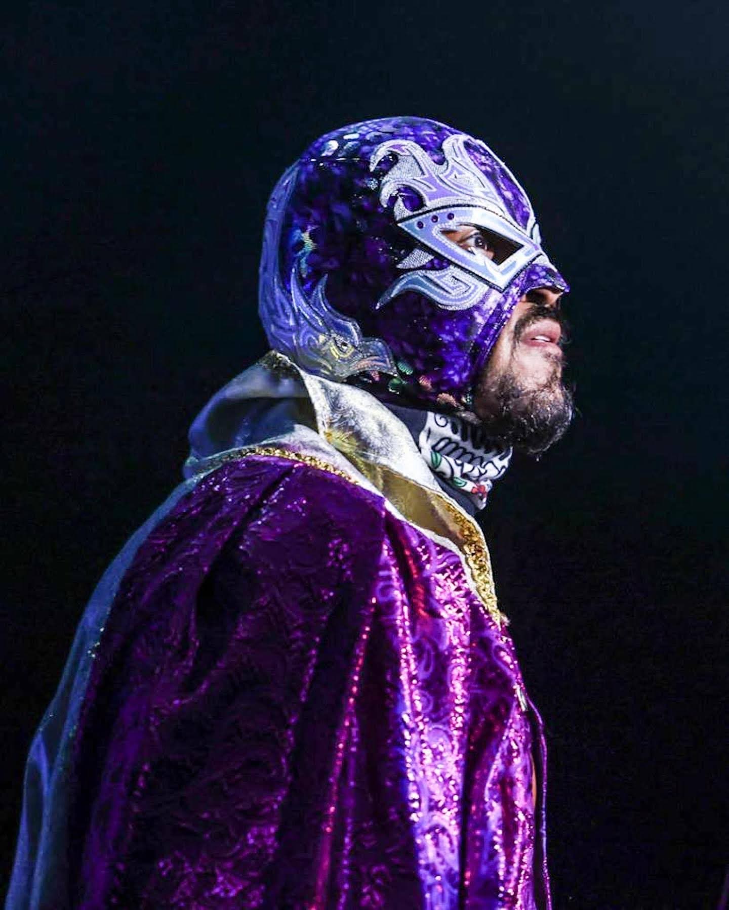 A luchador in an ornate purple and silver mask and matching shimmering purple cape.