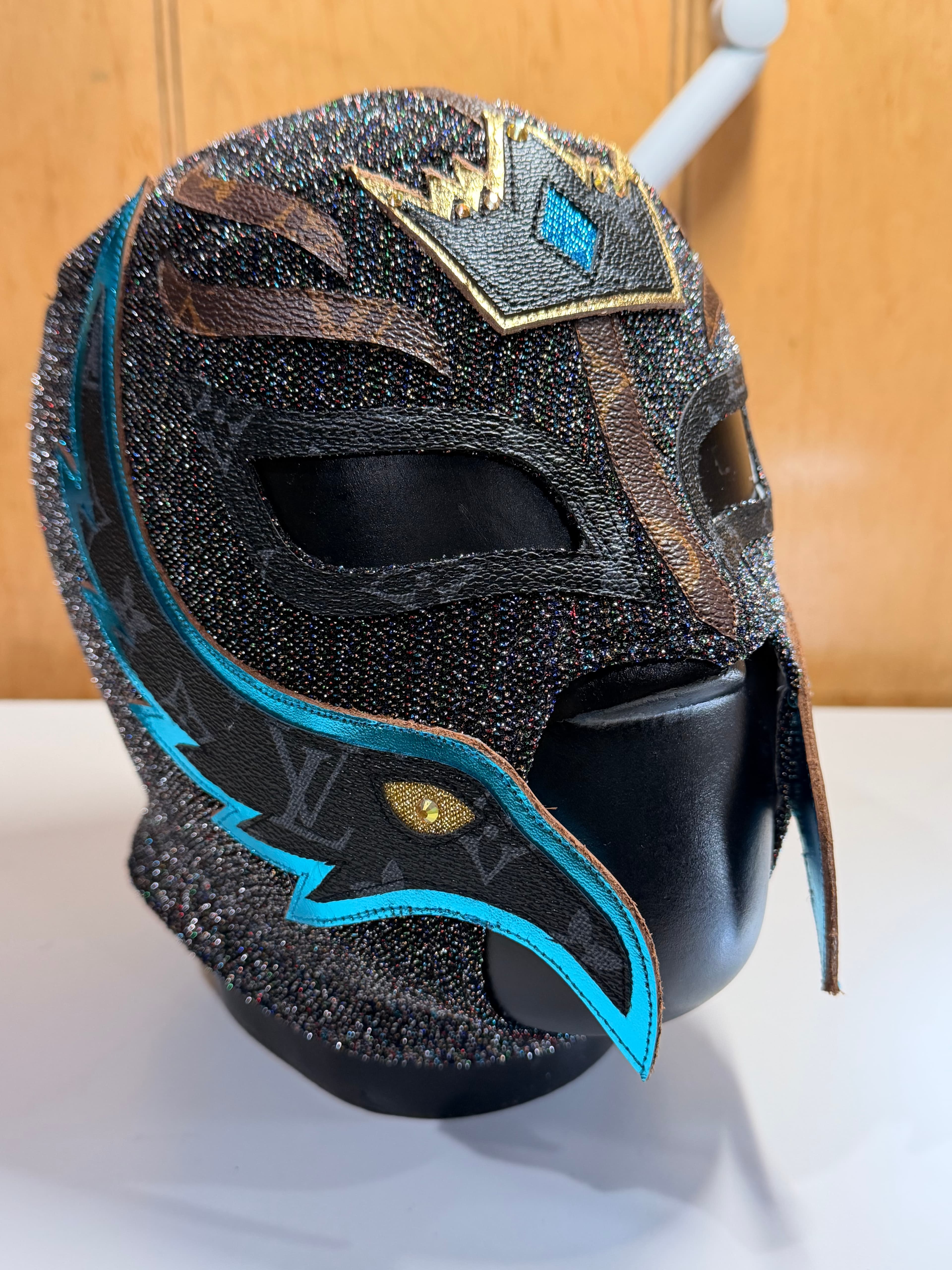 Detailed black sparkly luchador mask with blue trim and leather accents on a mannequin.